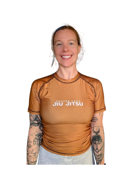 Coach Alli smiling and standing in her Sucker Free Jiu Jitsu nogi rashguard - brown belt ranked. 